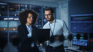 Two people solutions looking at a computer screen with a tech background